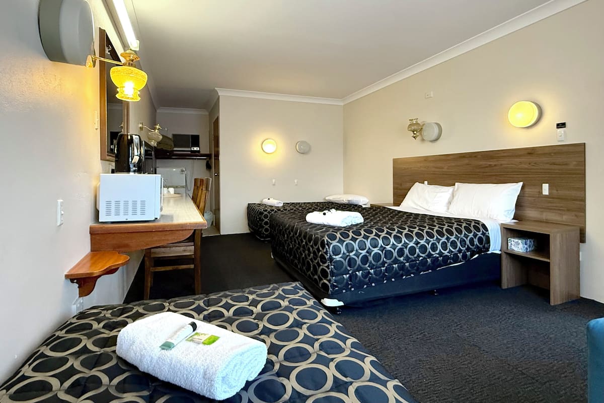 Habitación de hotel con dos camas, un escritorio con computadora, un espejo y una pequeña kitchenette.