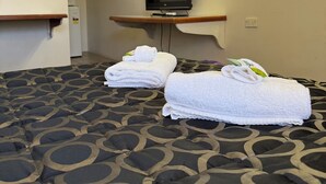 Hotellihuone, jossa on sänky, jalustalla oleva televisio, peili ja pieni pöytä, jonka päällä on pyyhkeitä.