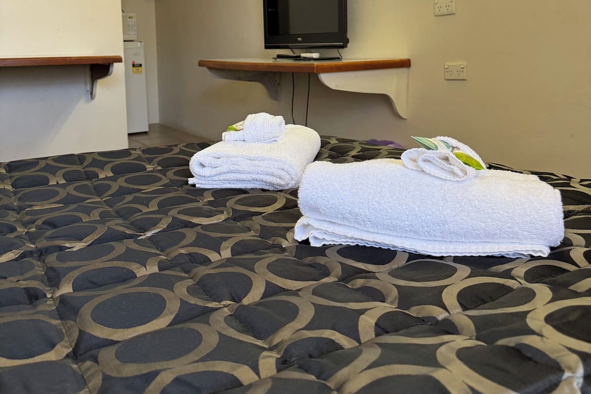 Una habitación de hotel con una cama, un televisor en un mueble, un espejo y una mesita con toallas.
