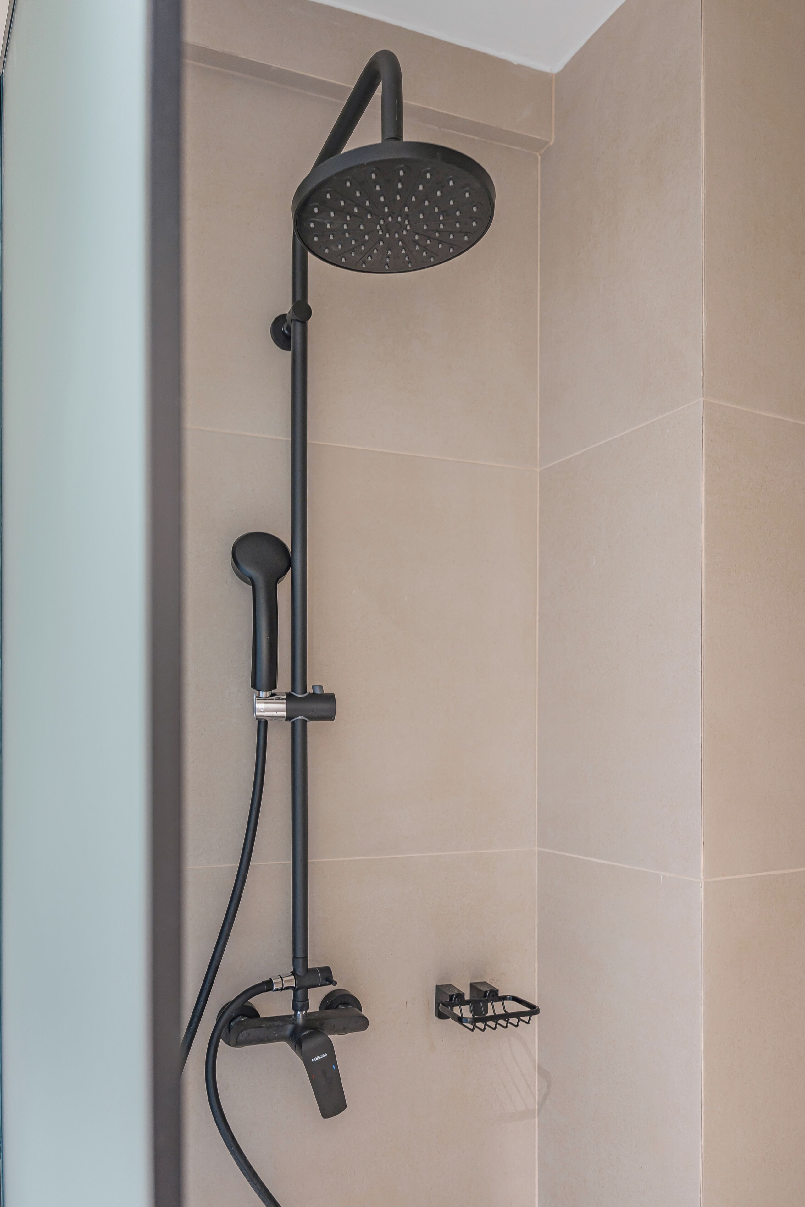 A modern shower with a handheld showerhead and a fixed rain showerhead, mounted on a wall with beige tiles.