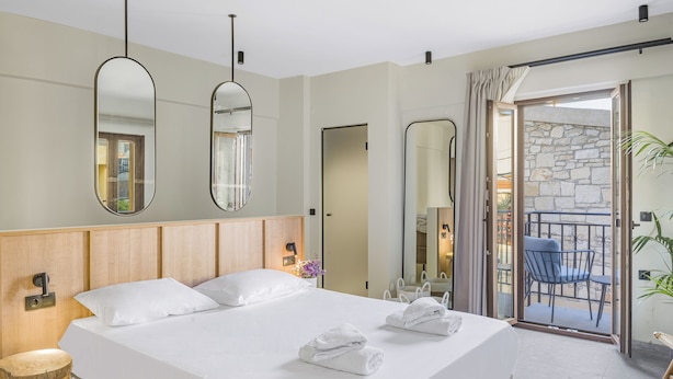 Et moderne hotelværelse med en stor seng, to sengeborde og en balkon med udsigt til en stenvæg og udendørs møbler.