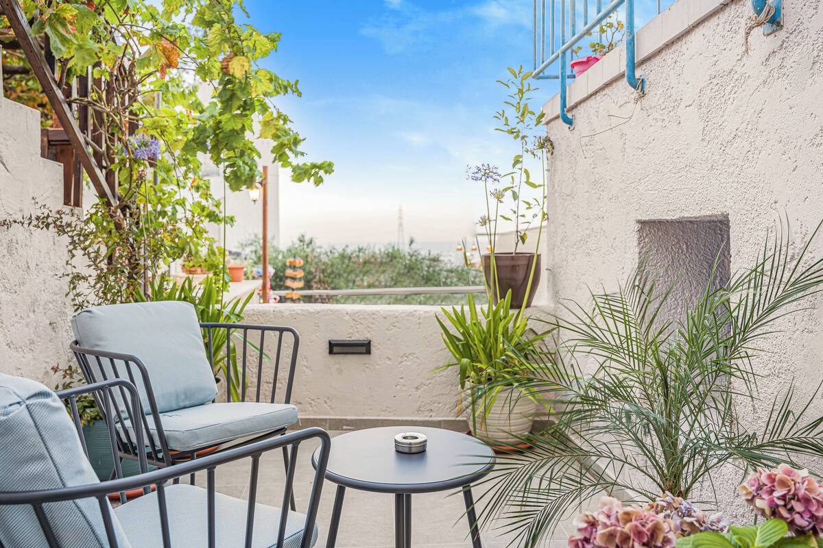 A patio with a table and chairs, surrounded by potted plants and a view of the cityscape.
