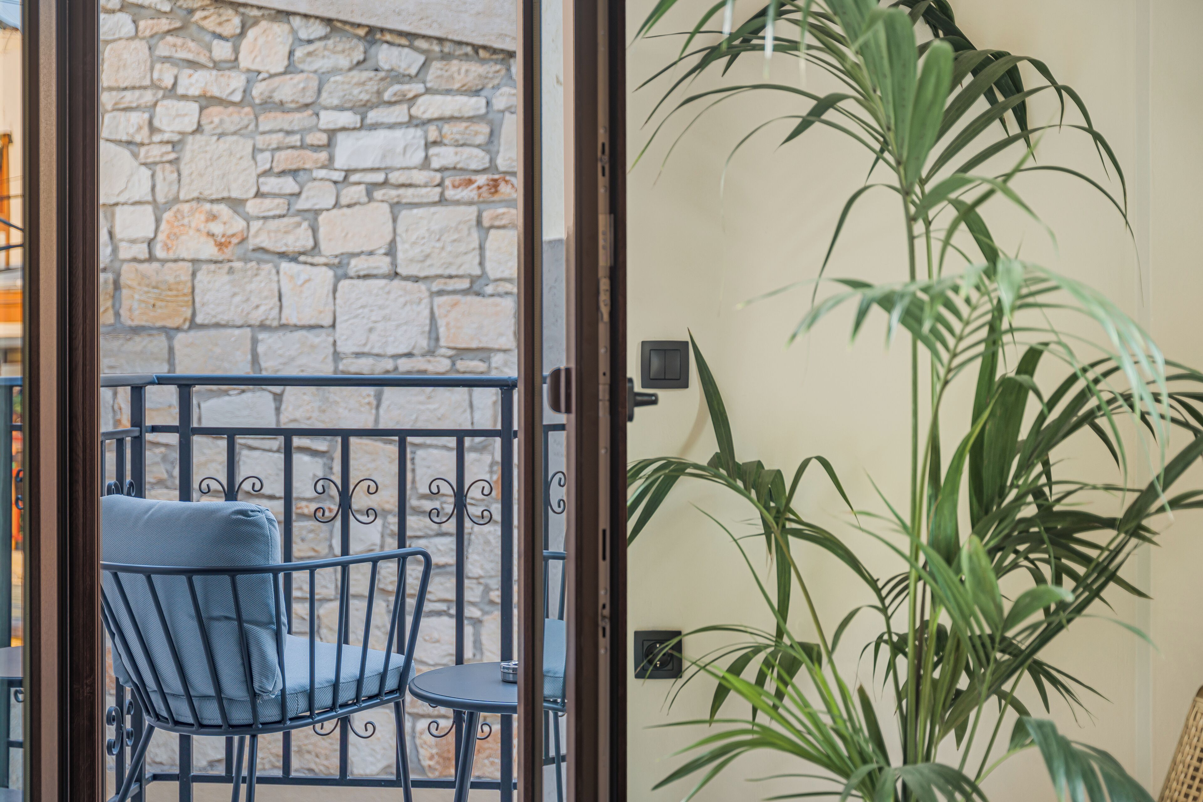 A balcony with a stone wall, a metal chair with a cushion, and a potted plant.