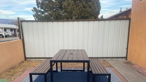 A picnic table with benches in a backyard with a white fence and a tree in the background.