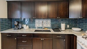 A kitchen with dark wooden cabinets, a granite countertop, a sink, and a backsplash with a blue and white pattern.