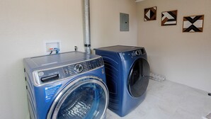 A laundry room with two blue washing machines and a metal exhaust pipe.