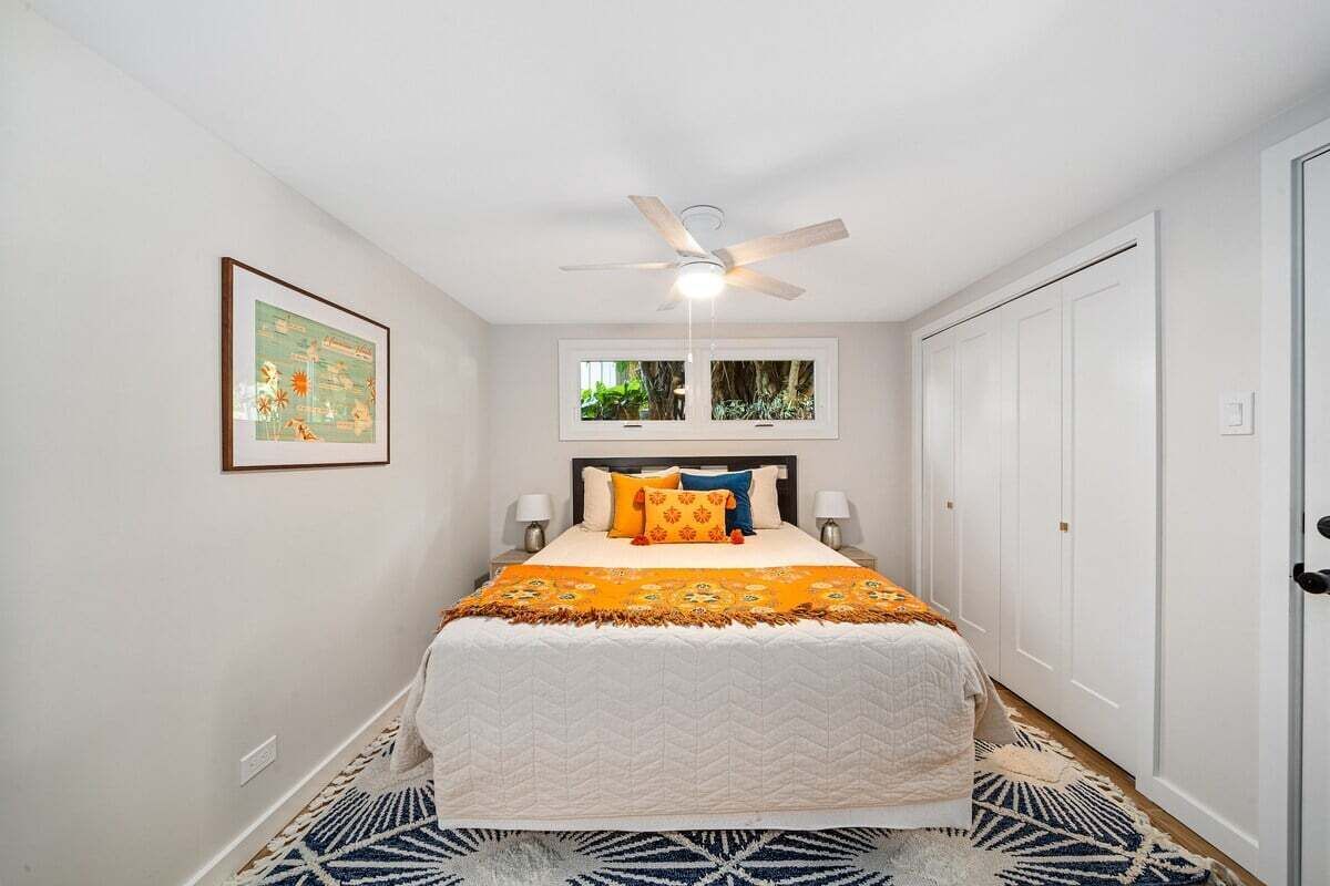 A bedroom with a bed, a ceiling fan, a window, and a door.