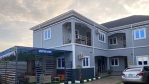 A two-story building with a reception lounge, a covered outdoor seating area, and a parked car. - Geoworld Apartments & Suites (Makurdi)
