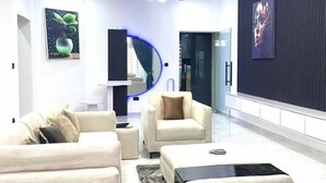 A modern living room with a sofa, armchair, and coffee table. There are two paintings on the walls and a blue circular light fixture. - Geoworld Apartments & Suites (Makurdi)