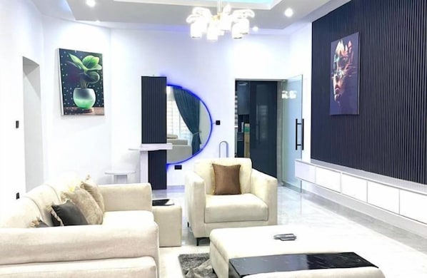 A modern living room with a sofa, armchair, and coffee table. There are two paintings on the walls and a blue circular light fixture.