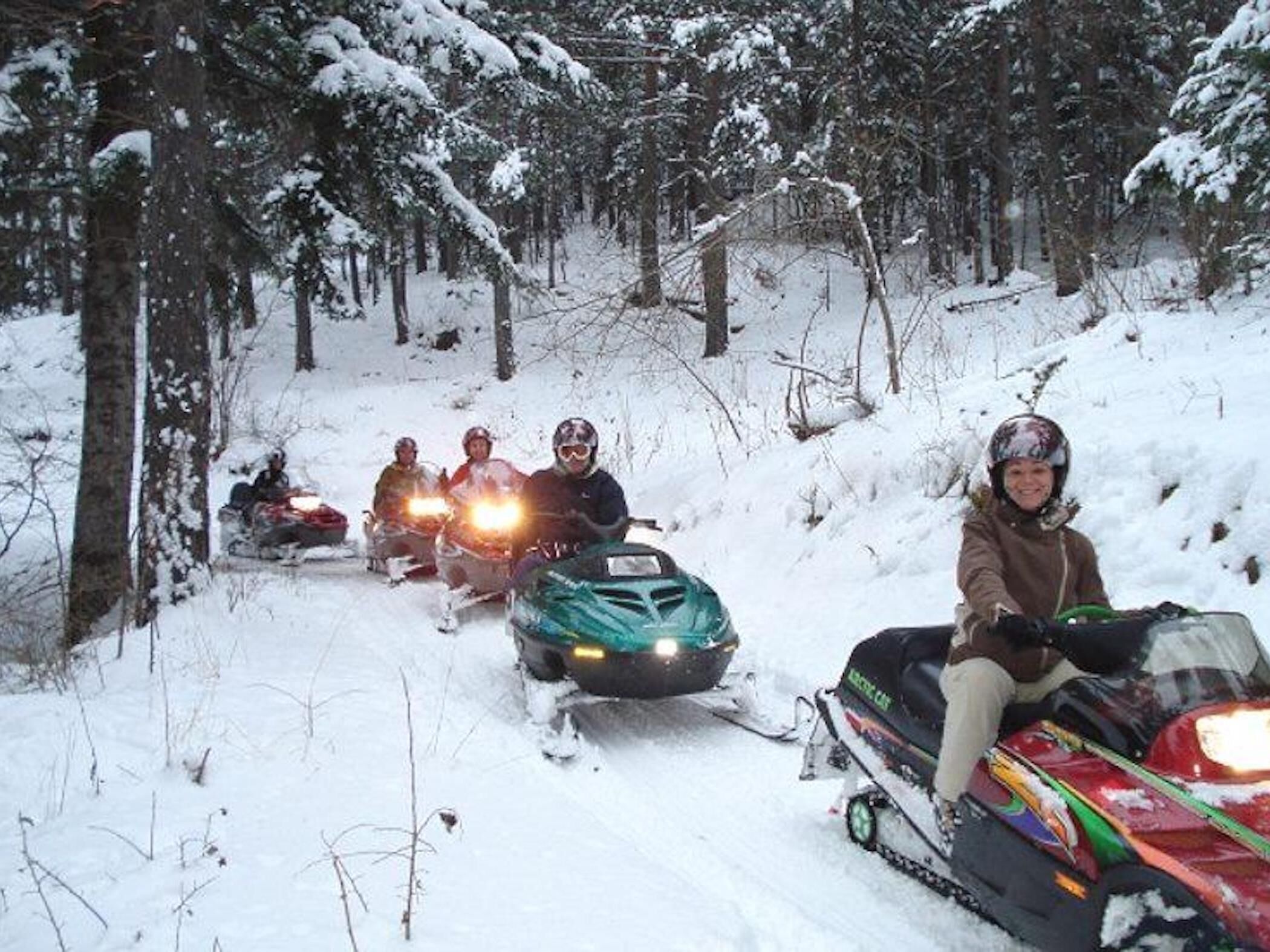 A group of people on snowmobiles in a snowy forest.