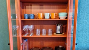 A wooden cabinet with shelves containing various glassware, plates, and a storage bin.