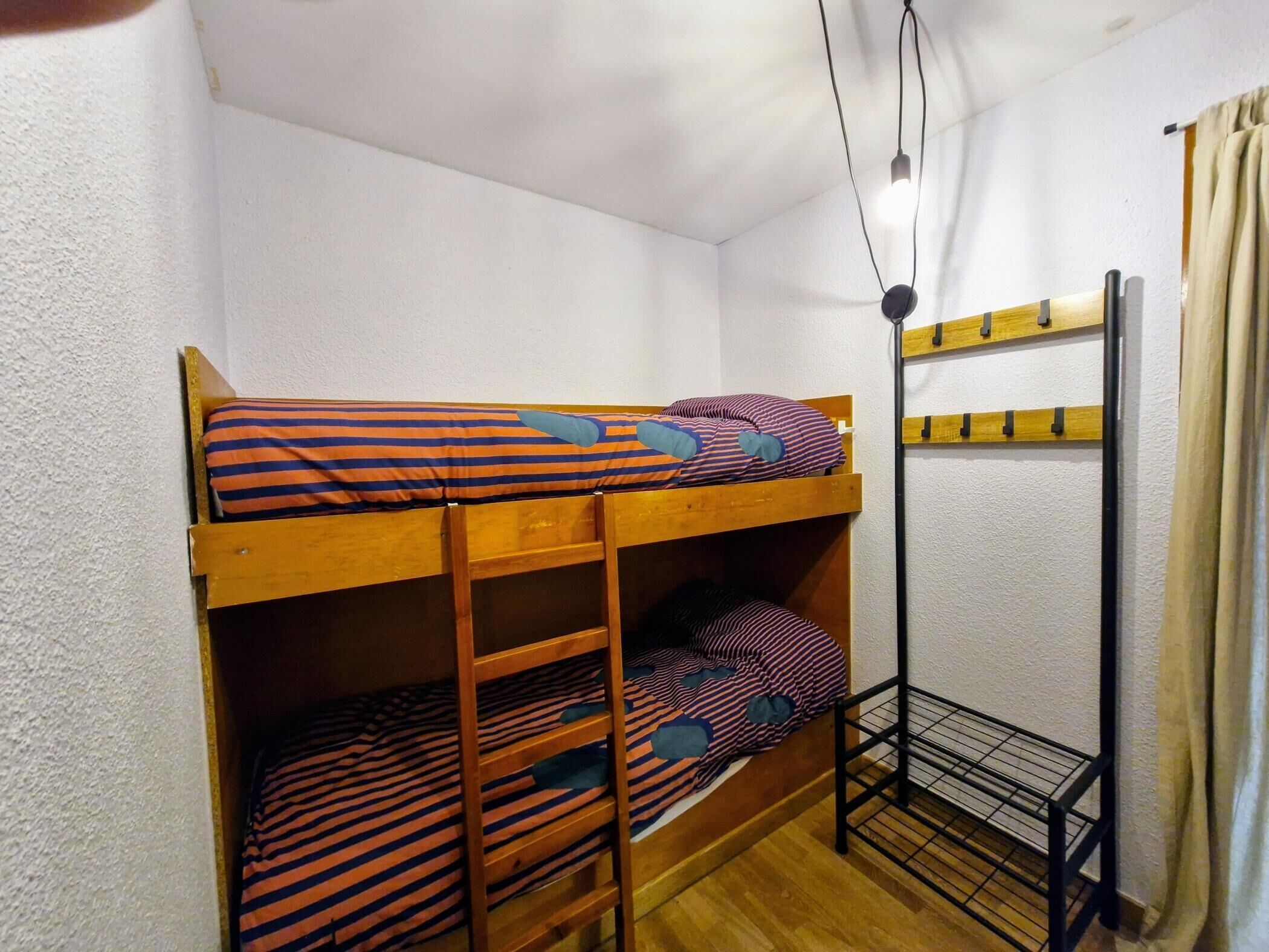 A bunk bed with striped bedding, a ladder, and a metal shelf unit against a white wall.