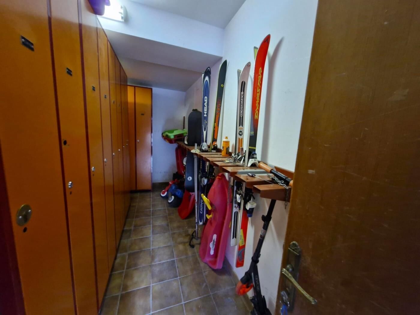 A hallway with lockers on the left and skis mounted on the wall.