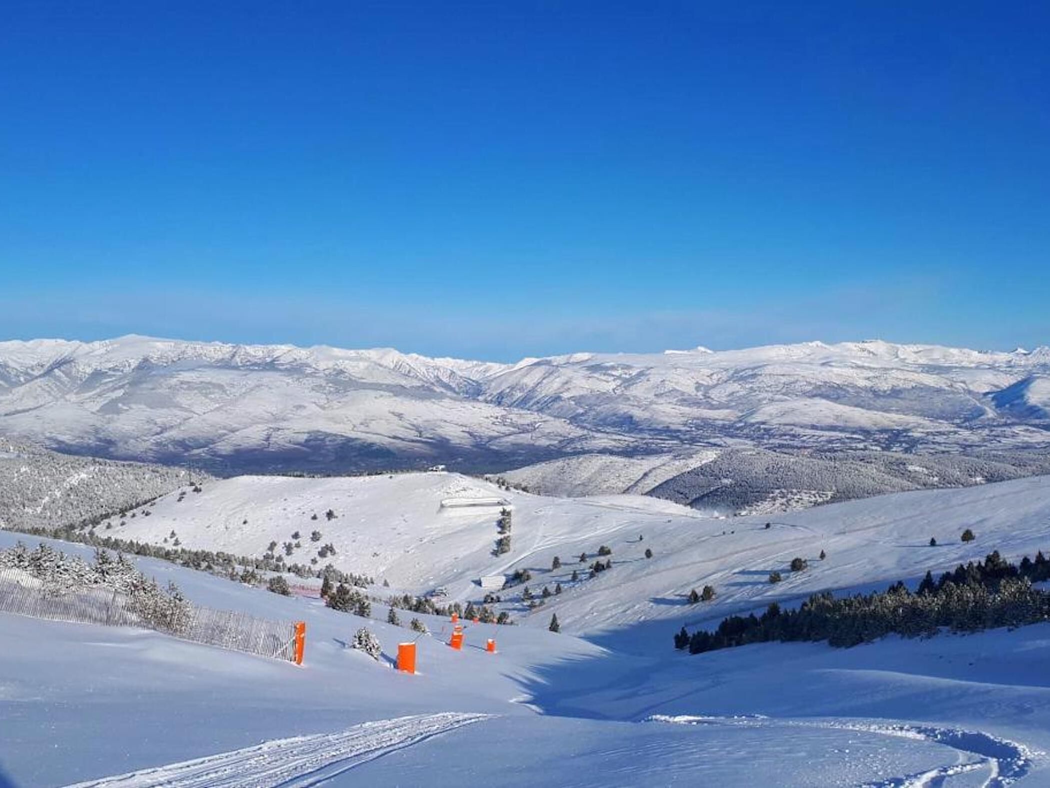 Paisaje montañoso cubierto de nieve con pistas de esquí y marcadores de seguridad anaranjados.