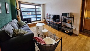 A living room with a dark sofa, a small round table, a TV, and a bookshelf.