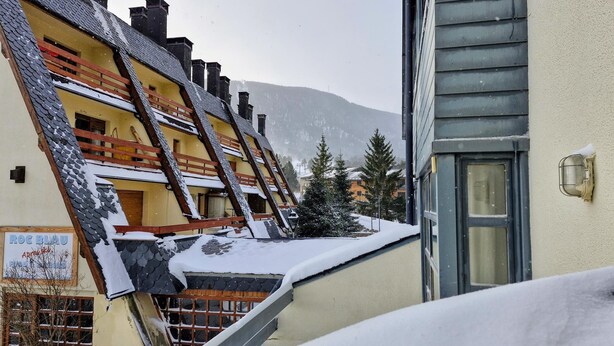A snow-covered building with a sloped roof and a visible staircase leading to a balcony.