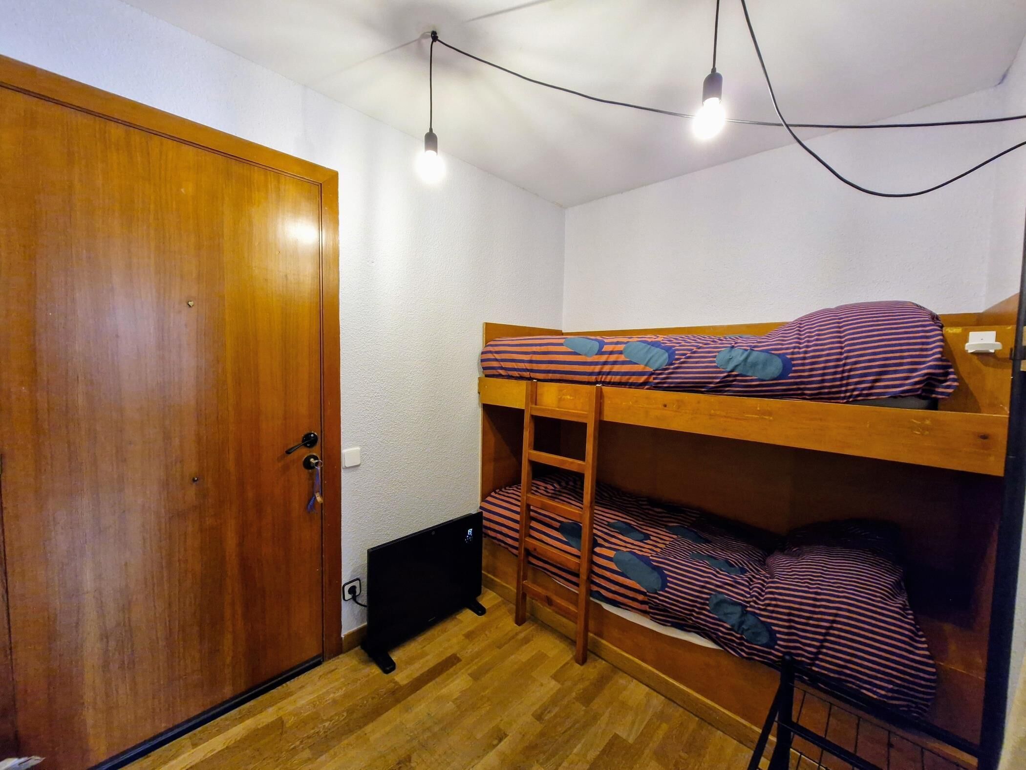 Una habitación pequeña con una cama nido, un armario de madera y un escritorio con una silla.