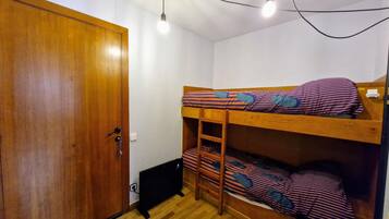 Una habitación pequeña con una cama nido, un armario de madera y un escritorio con una silla.