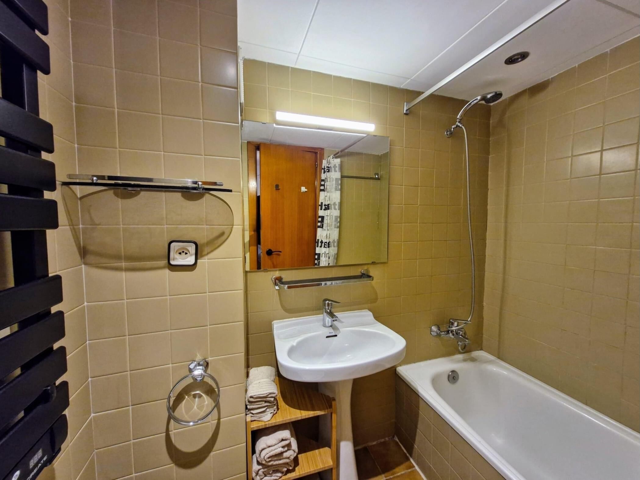 Un baño con lavabo, espejo y ducha. Hay toallas y un jabonera.
