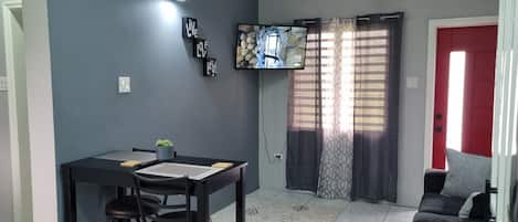 Um espaço de estar compacto com área de jantar, televisão na parede e uma porta vermelha.