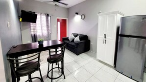 Une cuisine compacte comprenant un coin repas, un réfrigérateur, un ventilateur de plafond, un téléviseur fixé au mur et une porte rouge.