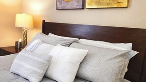 A neatly made bed with grey bedding and multiple pillows, a bedside table with a lamp, and two framed artworks on the wall. - Upgraded Vegas Oasis! Heated Pool, Hot Tub & Gym! (Las Vegas)