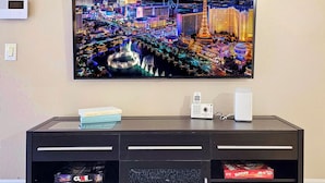 A flat-screen TV mounted on a wall above a black entertainment center with books and a remote control. - Upgraded Vegas Oasis! Heated Pool, Hot Tub & Gym! (Las Vegas)