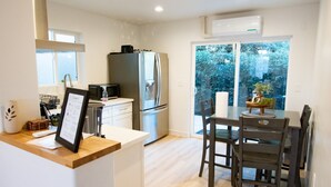 Una cocina moderna con armarios blancos, electrodomésticos de acero inoxidable y una zona de comedor con sillas y mesa de madera.
