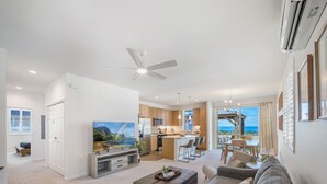 Una sala de estar moderna con un sofá, una mesa de centro y un televisor. Se observa una zona de cocina con una mesa de comedor y sillas.