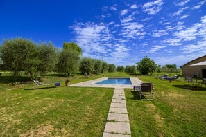 A backyard with a swimming pool, lounge chairs, and a stone pathway.