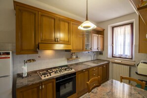 A kitchen with wooden cabinets, a gas stove, a sink, and a window with curtains.