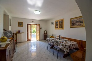 Un coin repas avec une table dressée pour quatre personnes, un ventilateur et une porte donnant sur l’extérieur.