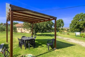 An outdoor patio with a wooden pergola, a table with chairs, and a hose on the ground.