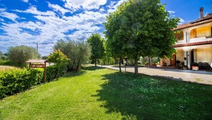 Ein gepflegter Garten mit verschiedenen Bäumen, einem gepflasterten Weg und einem Gebäude mit einem Ziegeldach.