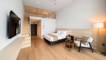 A modern hotel room with a bed, a chair, a TV, and a staircase leading to an upper level.