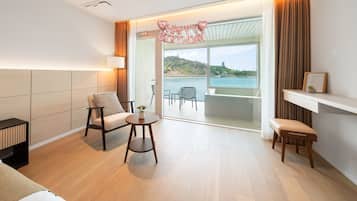 Habitación de hotel moderna con sofá, una mesita, un banco, una lámpara y vistas al mar a través de amplias ventanas.