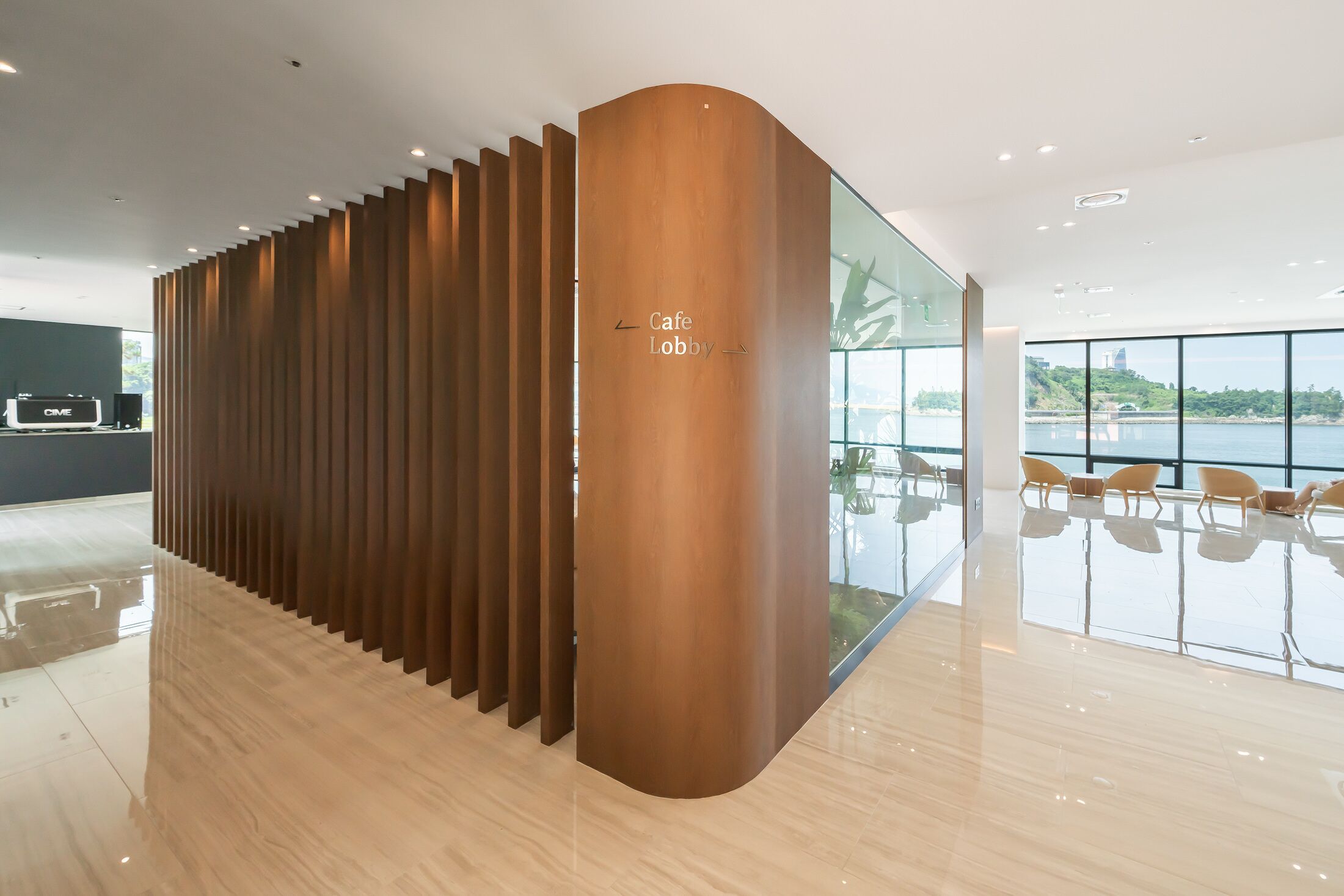 A modern lobby with a wooden partition, a glass wall, and a view of a body of water.