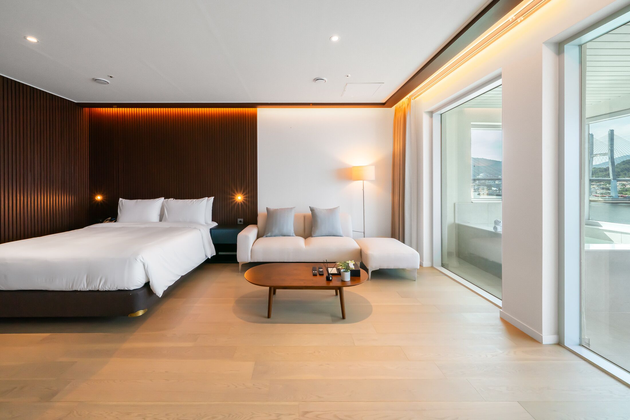 Una habitación de hotel moderna con una cama grande, un sofá, una mesita de café y vistas a un puente.