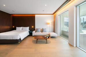 Una habitación de hotel moderna con una cama grande, un sofá, una mesita de café y vistas a un puente.