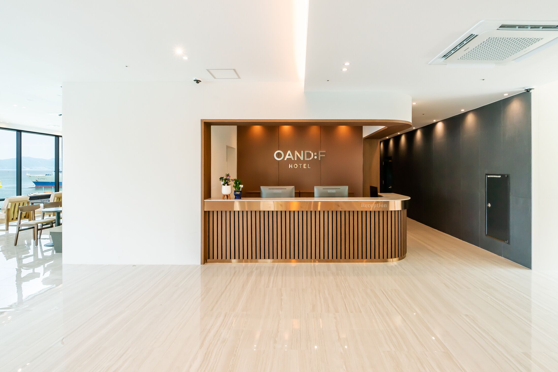 A modern hotel reception area with a wooden reception desk, a view of the sea, and a minimalist interior design.