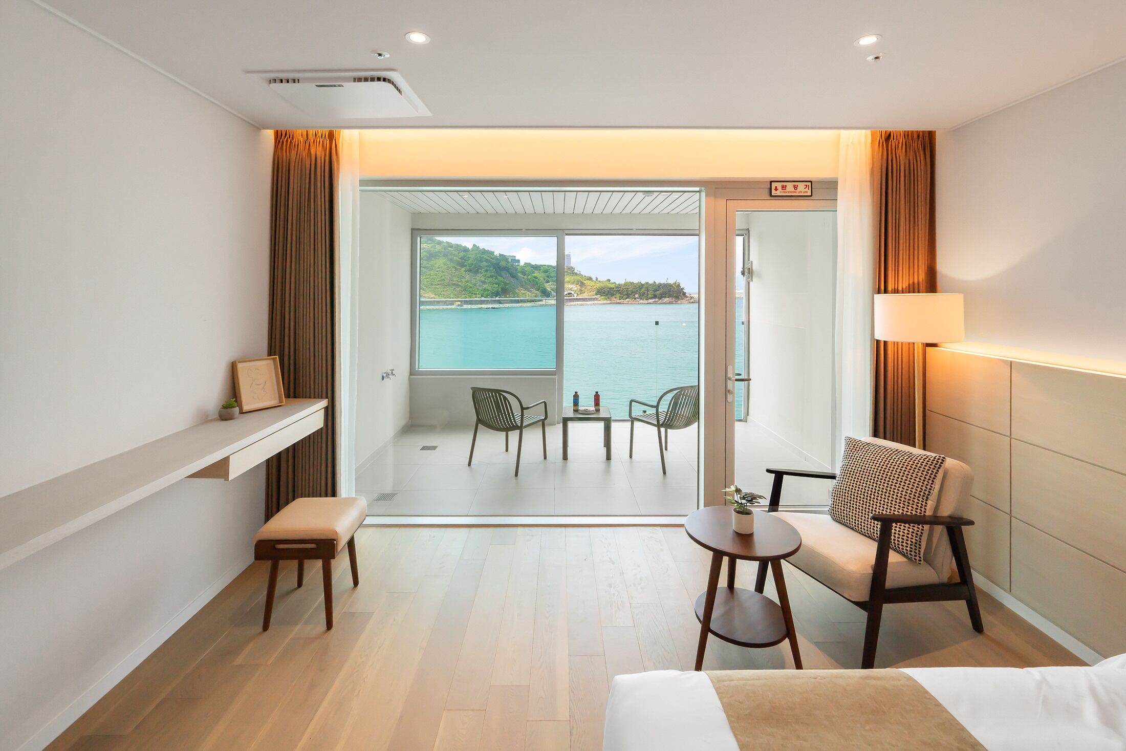 A hotel room with a balcony, a bed, a small table, a chair, and a sofa.