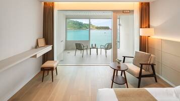 A hotel room with a balcony, a bed, a small table, a chair, and a sofa.