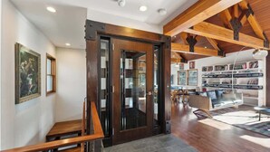 Un intérieur moderne avec un escalier en bois, une porte vitrée donnant sur une autre pièce et un espace de vie comprenant un canapé et des étagères.