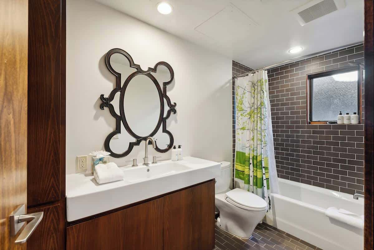 A bathroom with a wooden vanity, a large mirror, a toilet, and a bathtub.