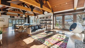 Un vaste espace de vie doté d’un plafond haut, de poutres apparentes, d’une table à manger, d’un canapé et d’un tapis aux couleurs vives.