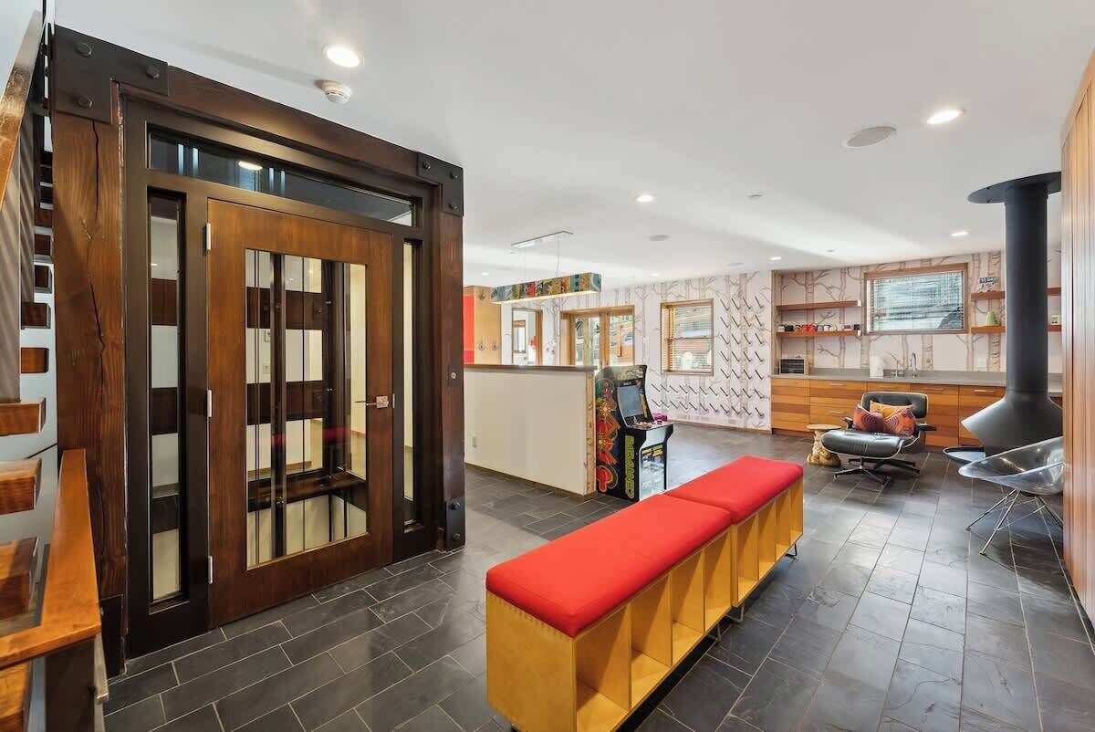 A modern interior with a wooden door, a bench, a fireplace, and a kitchen area.