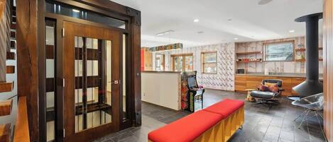 A modern interior with a wooden door, a bench, a fireplace, and a kitchen area.