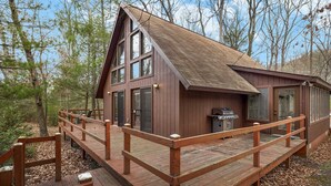 A cabin with a wooden deck, large windows, and a grill outside. - Loft, Wood Stove, Fire Pit, Grill & Deck on Creek (Hedgesville)