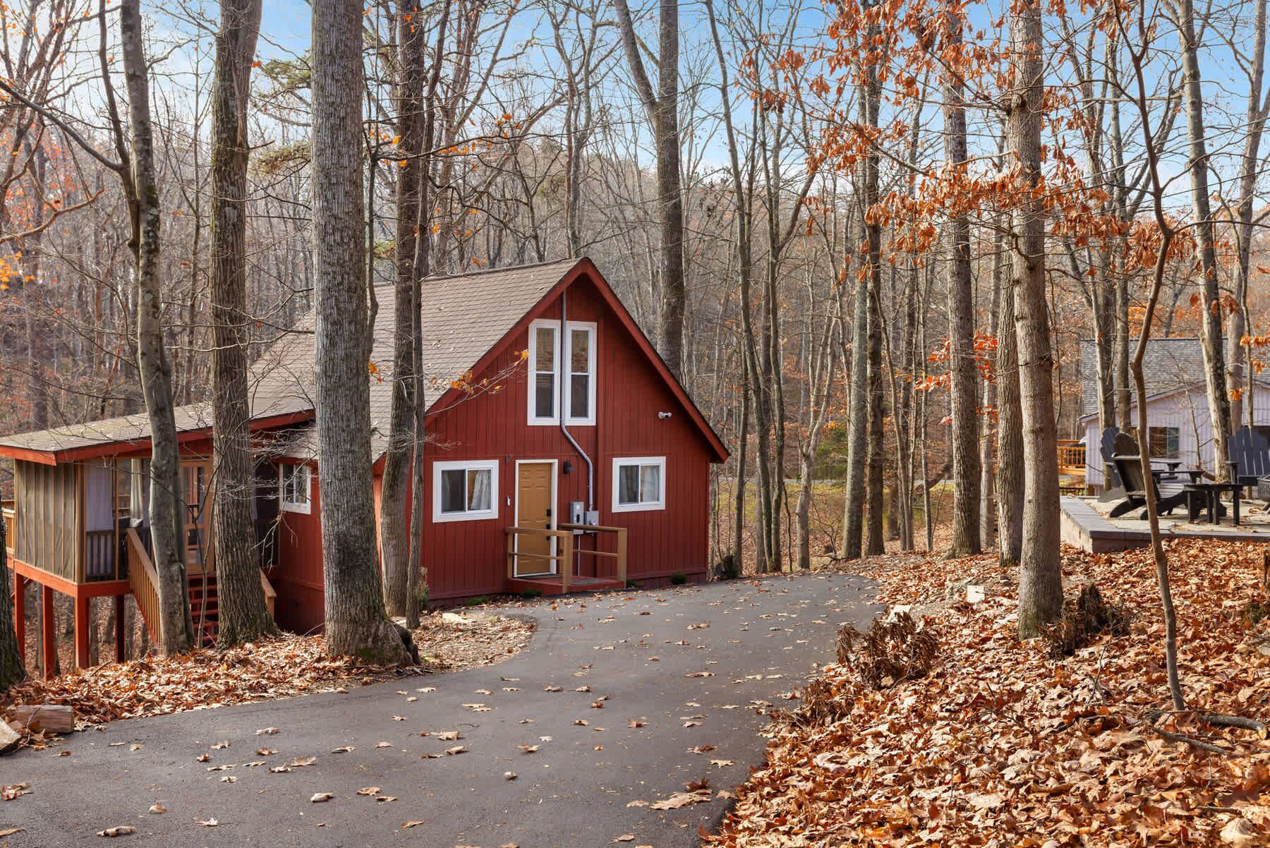 A red cabin with a front porch, surrounded by trees and a covered deck area.
